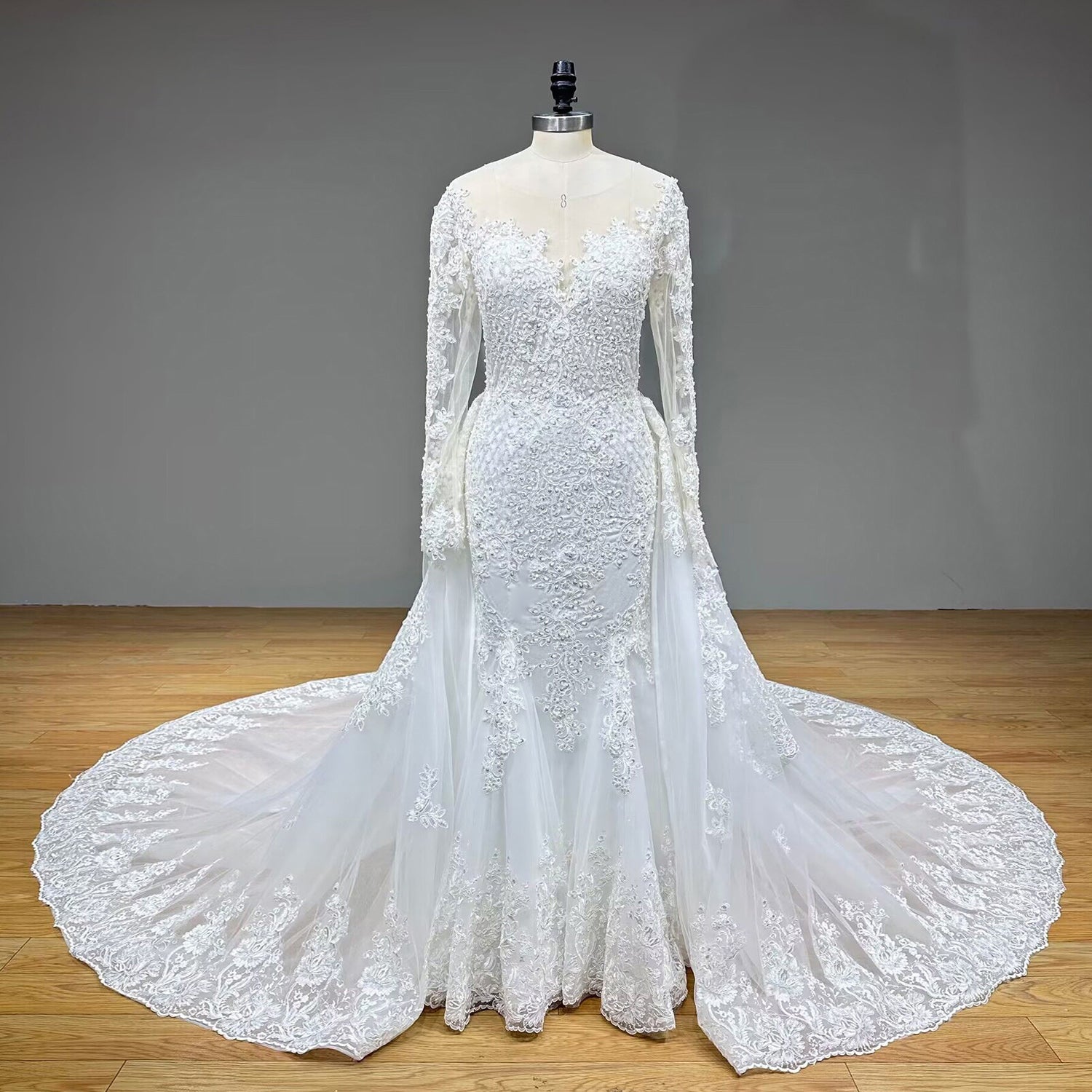 Full front display of a vintage 2-in-1 long sleeve mermaid wedding gown with its dramatic tulle and lace detachable overskirt train attached, on a studio mannequin.