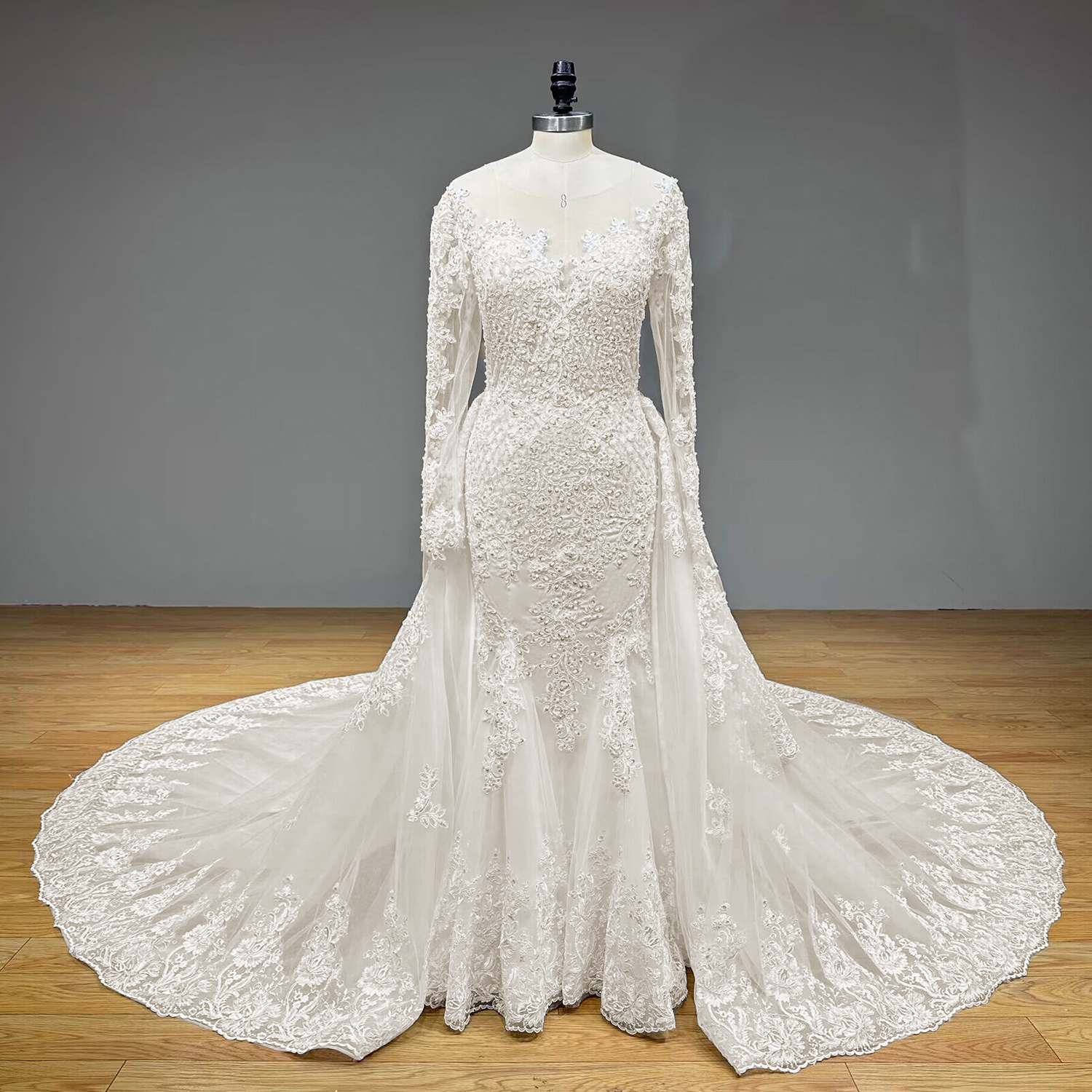 Video frame highlighting the front view of a luxury long-sleeve trumpet bridal dress with an illusion plunging neckline and a voluminous fanned-out detachable train.