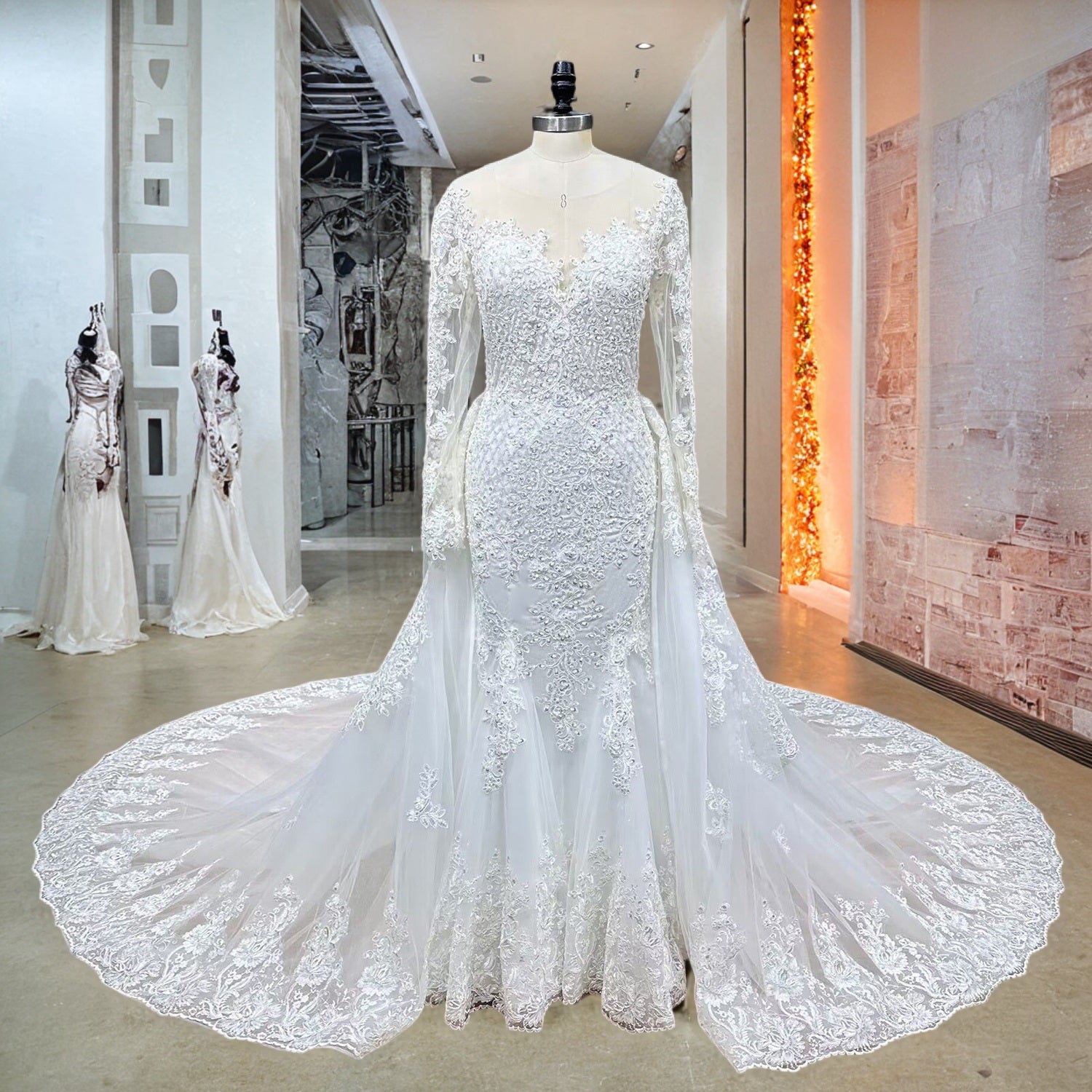 Full-length front display of an ivory long sleeve mermaid wedding dress with a sweeping detachable lace train on a boutique showroom mannequin.
