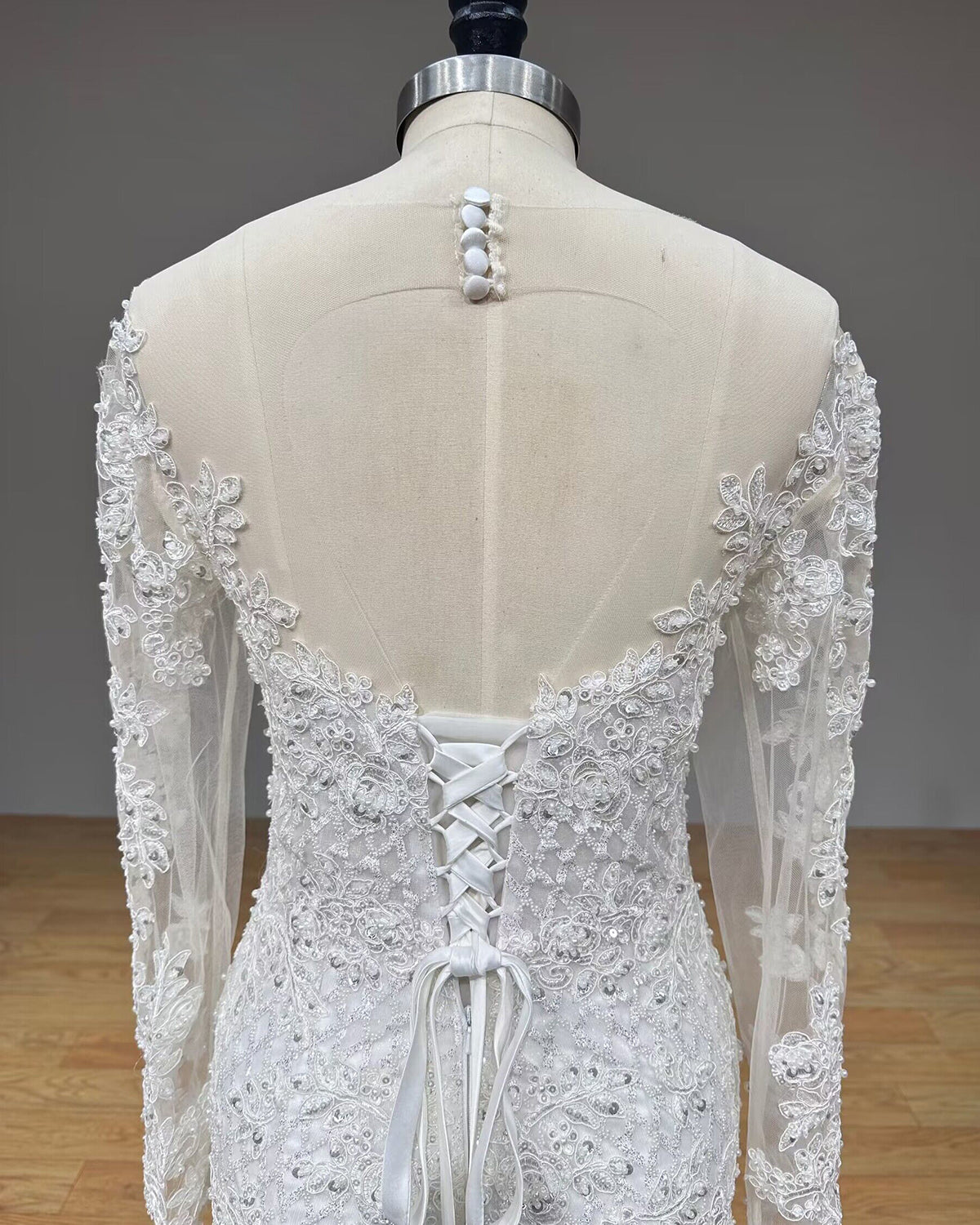 Close-up back view of the bridal bodice on a mannequin, showcasing the sheer mesh upper back with fabric buttons and an adjustable lace-up corset back closure.
