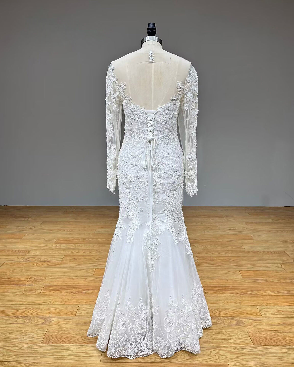 Full-length back view of the long sleeve lace mermaid wedding dress on a mannequin without the train, highlighting the sleek fitted trumpet silhouette.