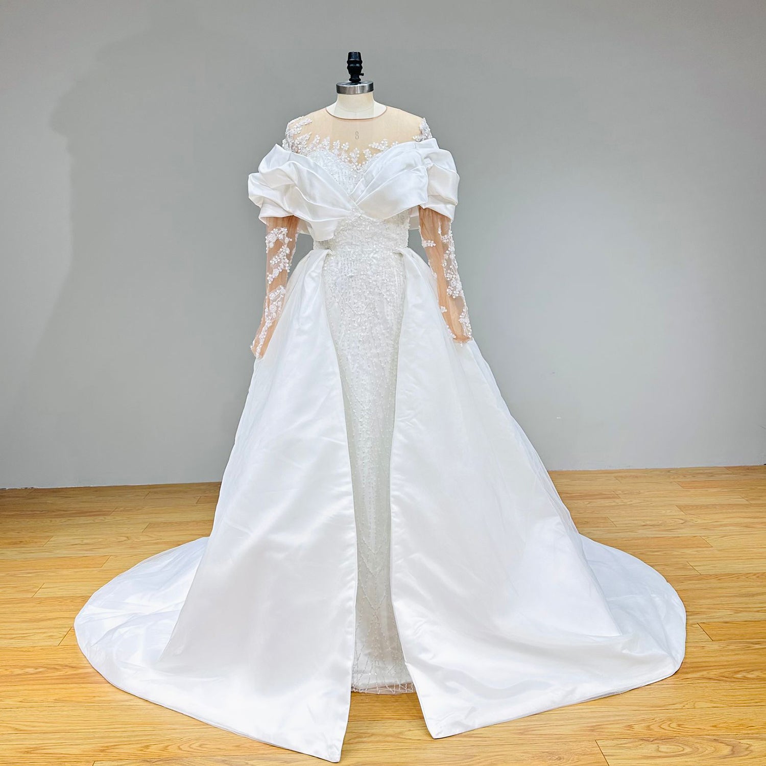 Front view of a convertable lace mermaid wedding dress displaying the grand satin overskirt train and an illusion neckline on a dress form.