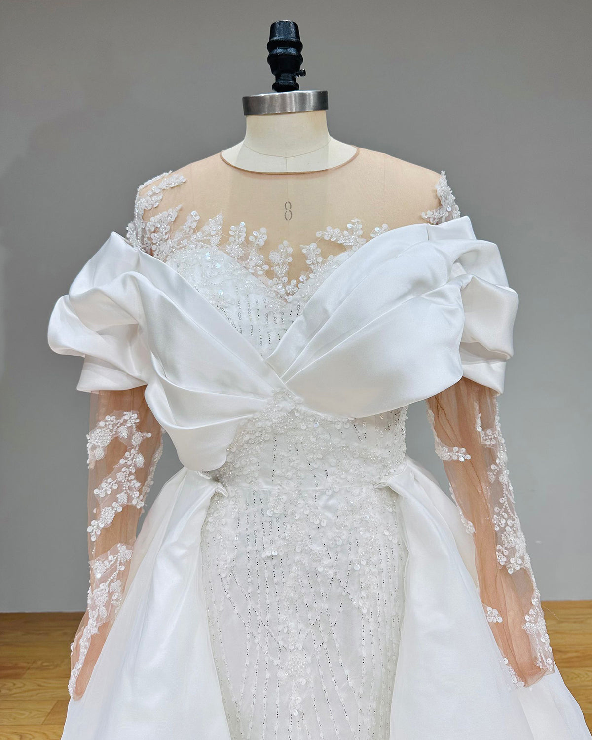 Close-up of a bridal bodice emphasizing the architectural cuffed portrait neckline, sequined mesh overlay, and detailed sleeve embroidery.