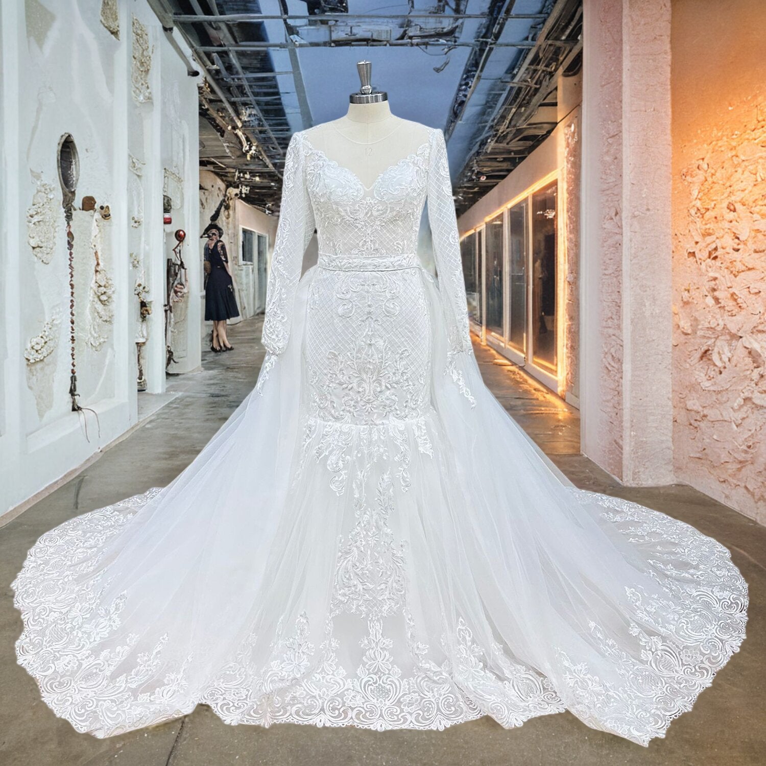Full front view of a long-sleeve trumpet wedding dress on a mannequin, highlighting the crosshatch lattice embroidery and scalloped lace hemline of the attached overskirt.