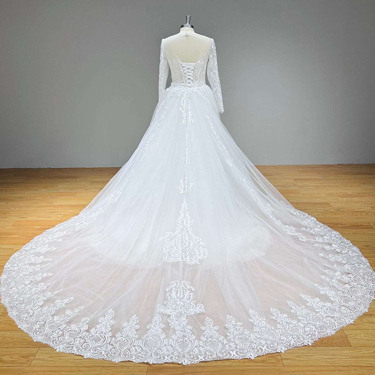 Full back view of a lace mermaid bridal gown on a dress form, displaying an open keyhole cut-out back, a lace-up corset midsection, and an embroidered tulle cathedral train.