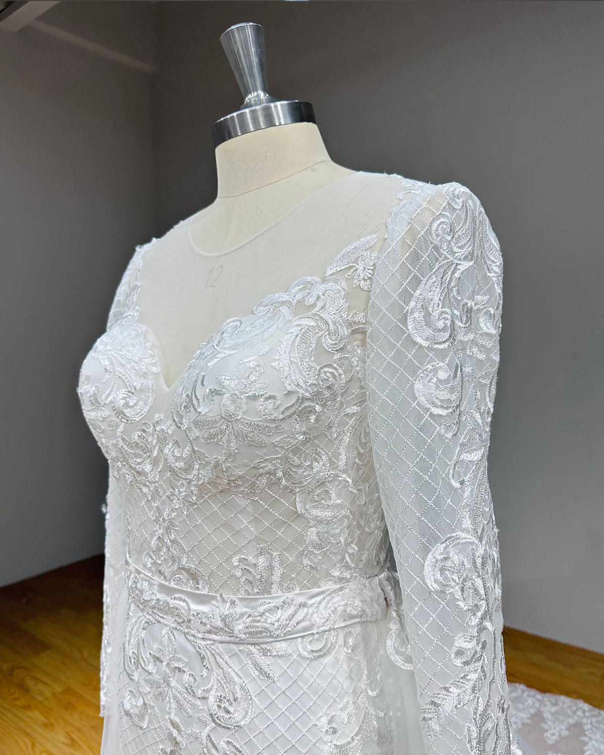 Side profile detail of a long-sleeve lace wedding dress on a mannequin, showcasing the seamless transition of the floral embroidery from the shoulder down the sleeve.