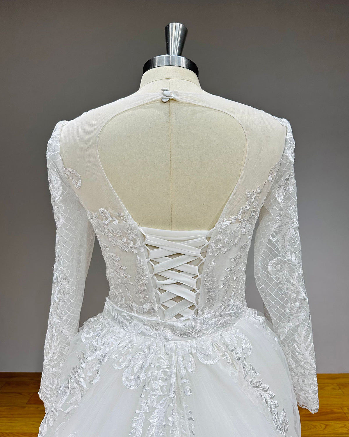Close-up back detail of a wedding dress featuring a sheer mesh illusion upper back, a round keyhole cut-out, an adjustable satin lace-up closure, and a defined waistband.