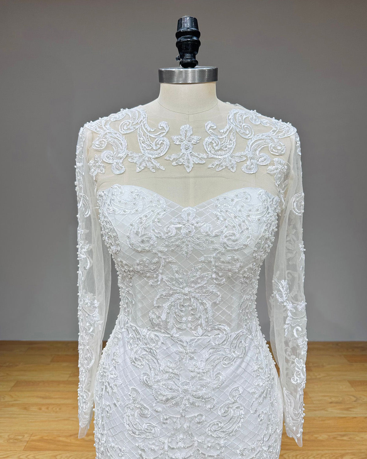 Detailed close-up front view of the wedding dress bodice showcasing the sheer high-neck lace overlay with intricate pearl appliques over a sweetheart neckline.