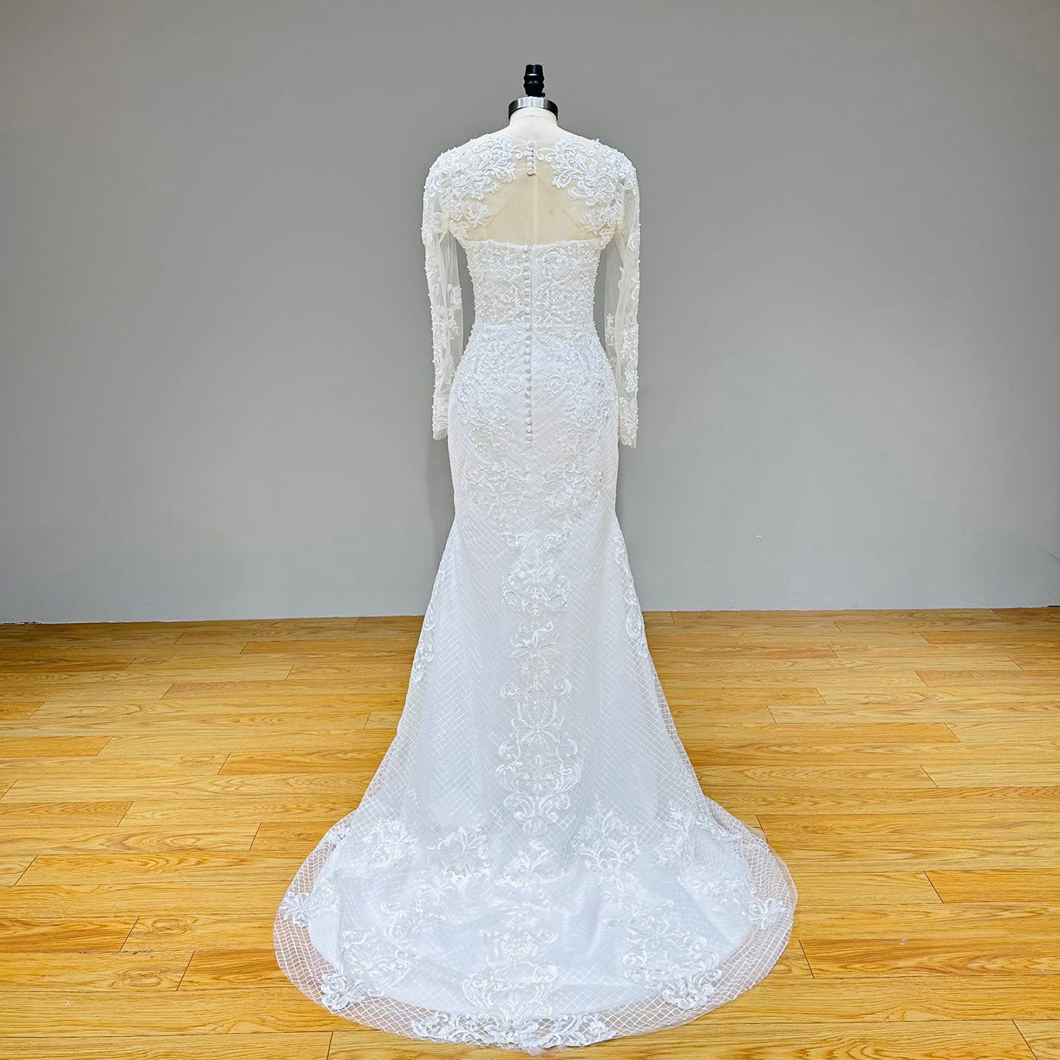 Full-length studio back view of the lace mermaid bridal gown on a mannequin, highlighting the button-up sheer back jacket and an elegant circular lattice lace train.