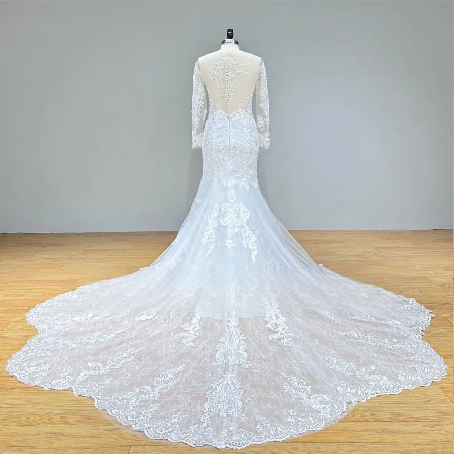 Detailed view of the back of a wedding dress on a mannequin, showing the sheer illusion back with a row of elegant pearl buttons and intricate lace embroidery.