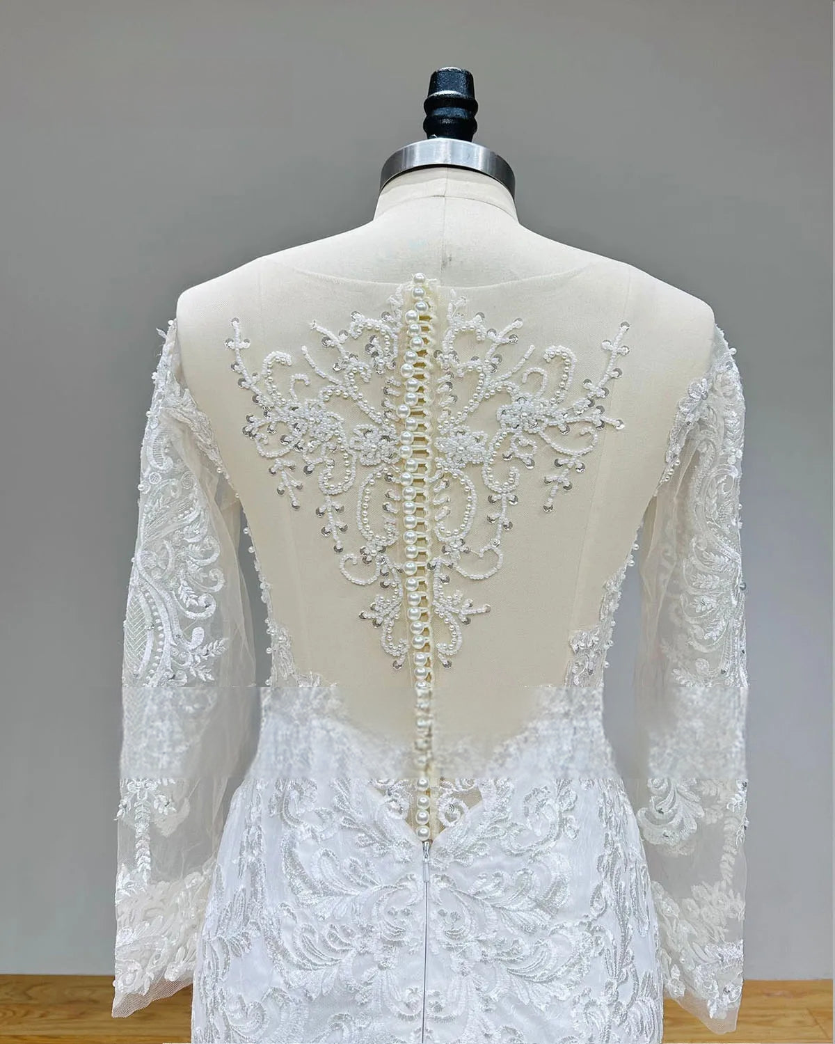 Close-up of the pearl back beading and floral lace appliques on the sheer illusion back of a long-sleeve mermaid wedding gown.