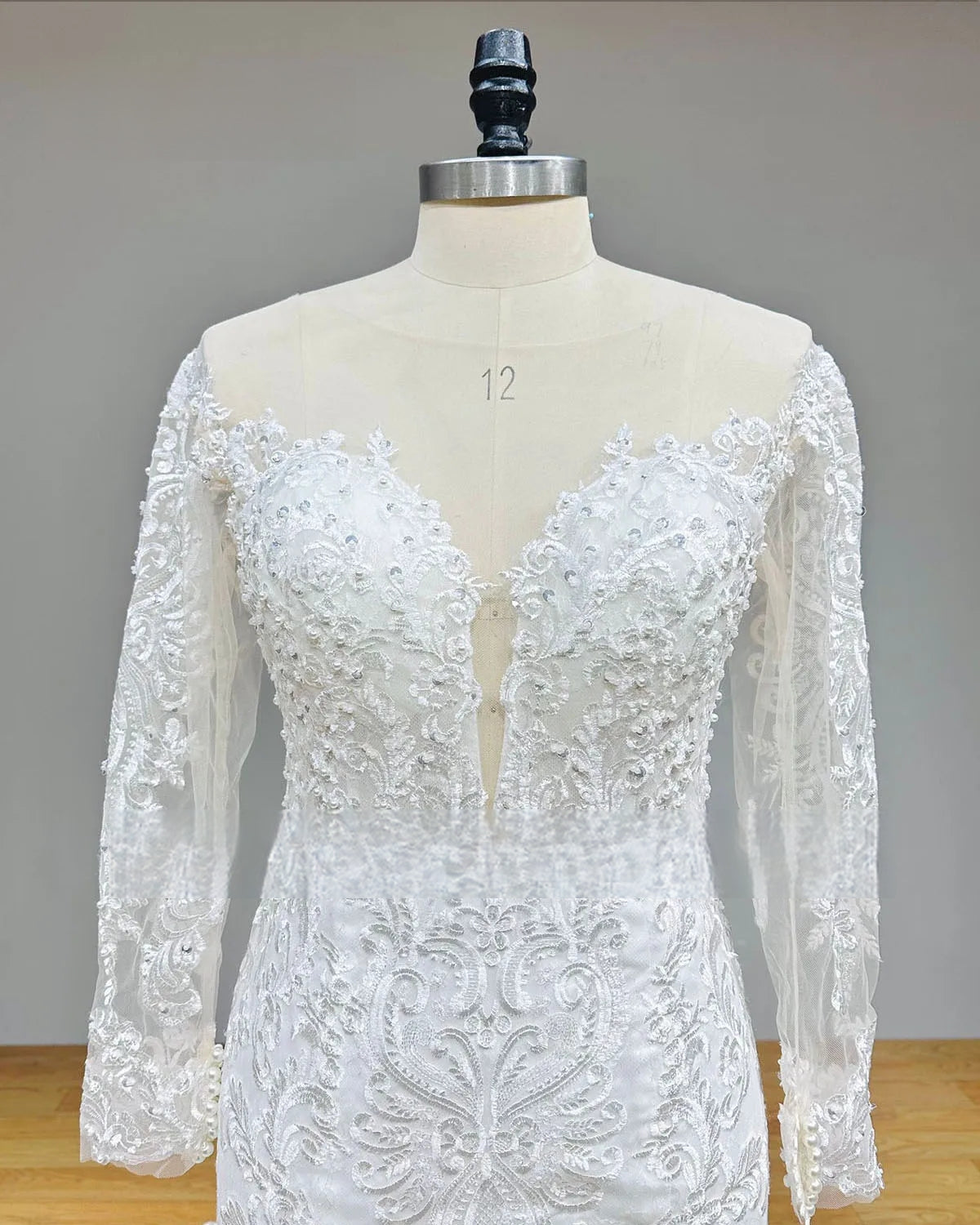 Detailed view of the back of a wedding dress on a mannequin, showing the sheer illusion back with a row of elegant pearl buttons and intricate lace embroidery.