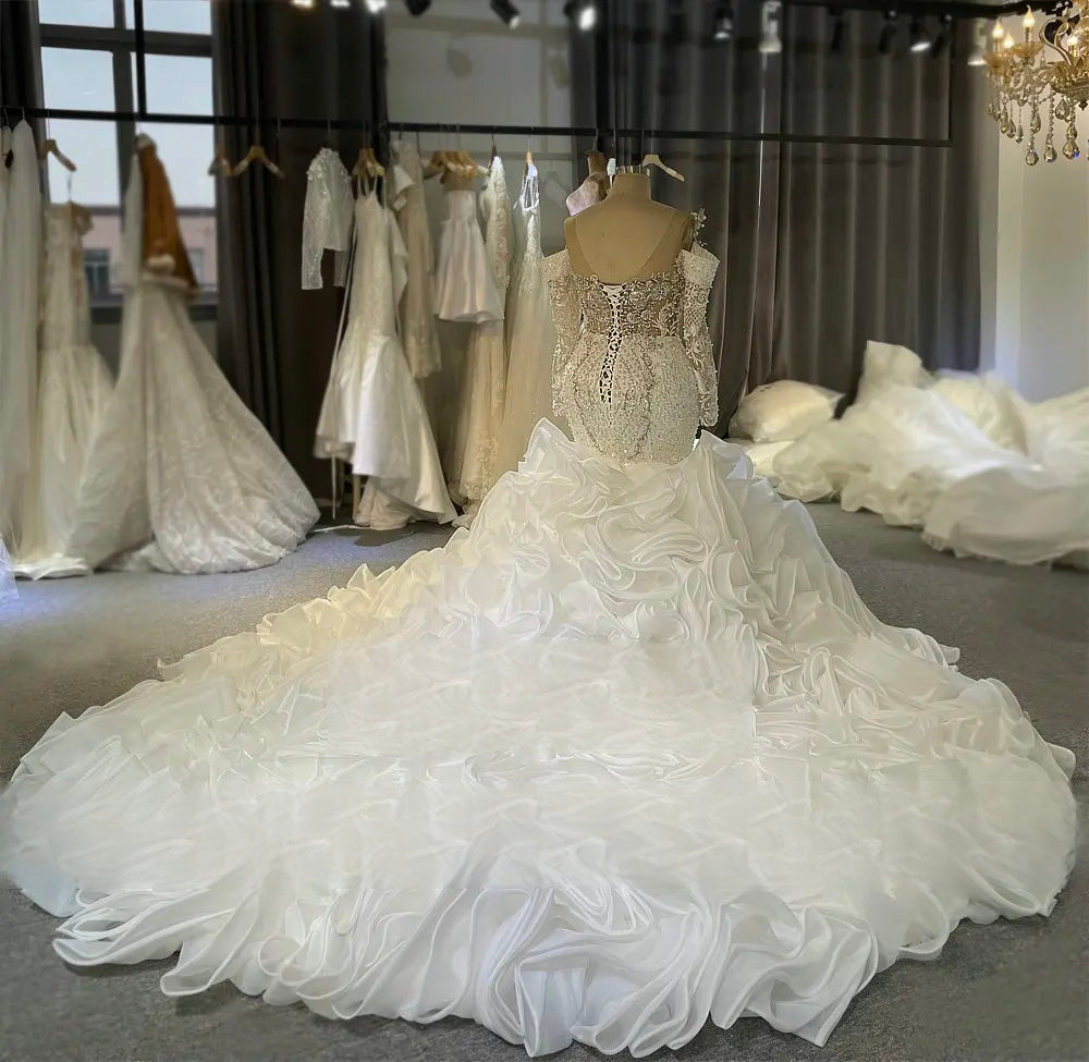 Back view of a mermaid wedding gown showcasing a dramatic and expansive ruffled train, low back with corset lacing, and long sleeves.