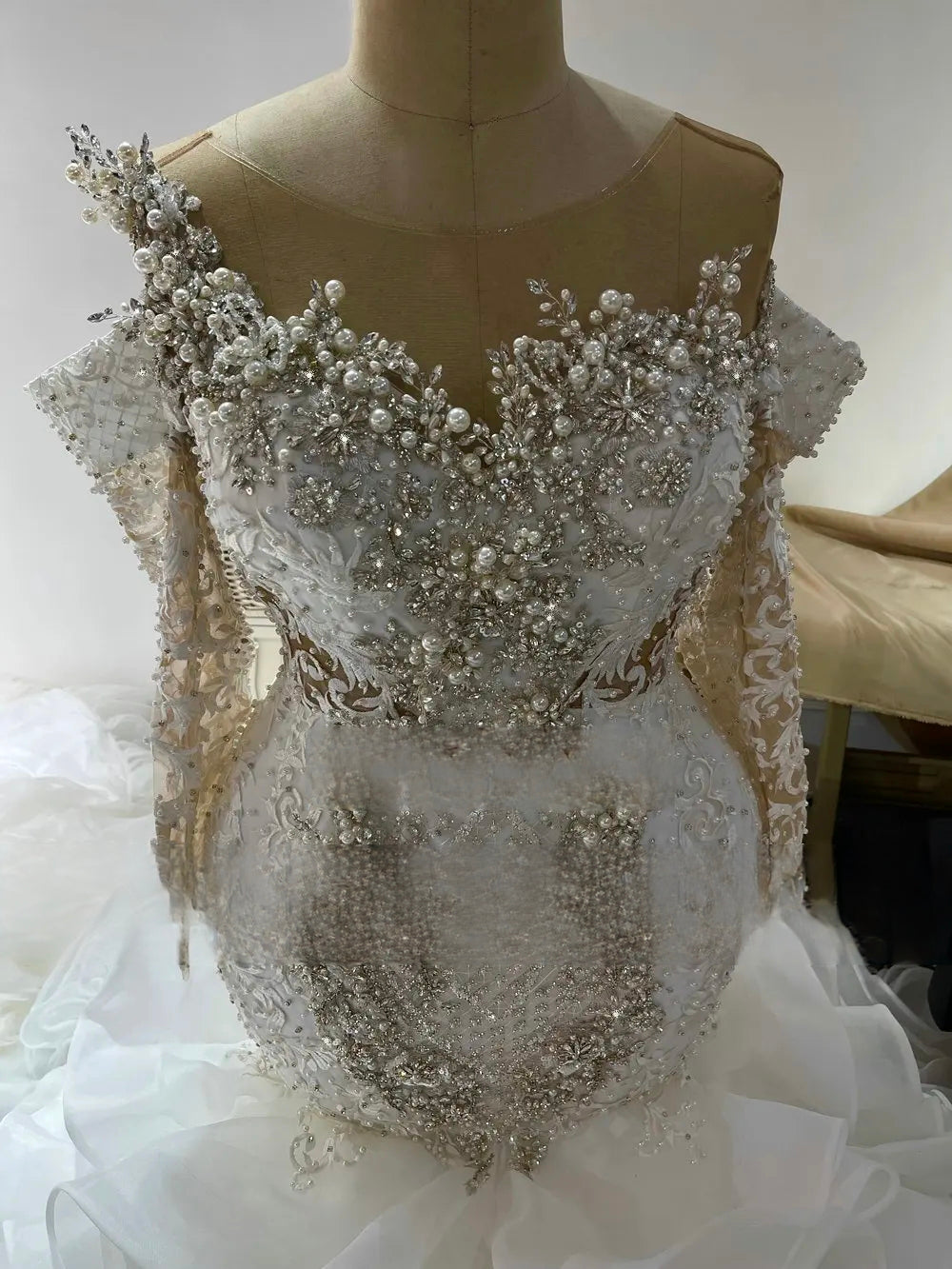 Close-up detail of the 3D crystal and pearl beaded bodice of a luxury mermaid wedding dress, highlighting intricate hand-stitched patterns and sheer long sleeves.