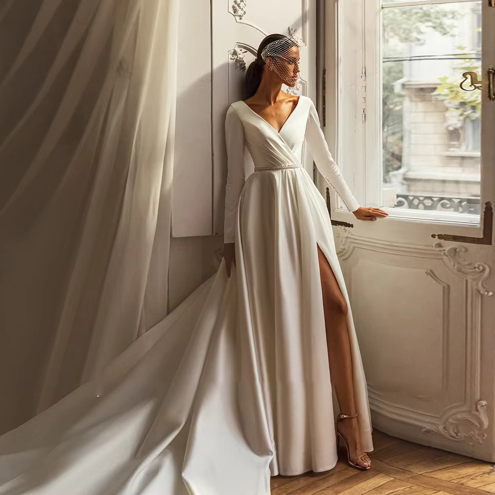 Modern satin bridal dress with a leg slit and sweeping train, worn by a bride posing by a classic window wearing a vintage birdcage veil.
