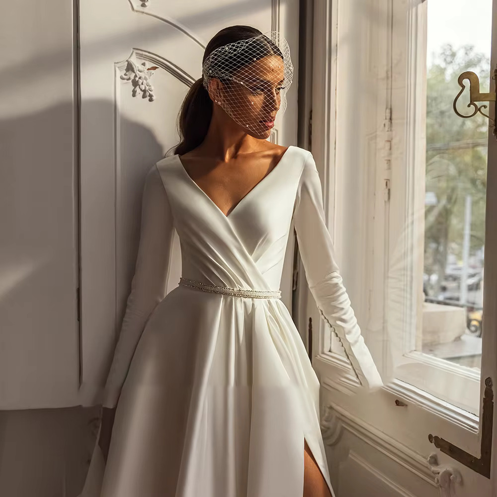 Close-up of a long sleeve ivory silk wedding dress bodice featuring pleated surplice draping and a delicate crystal-beaded waistband.