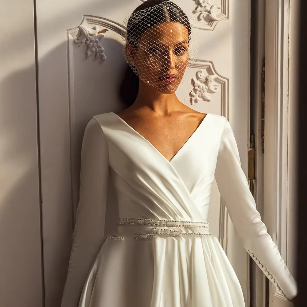 Detailed view of a thin luxury bridal belt made of crystal beads and freshwater pearls on a pleated white satin wedding dress.