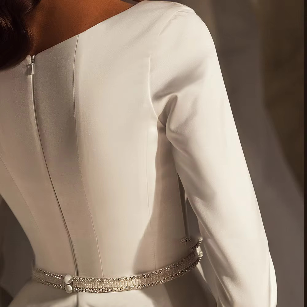 Close-up rear angle of a clean-cut satin wedding gown showing a hidden zipper closure and the back of a pearl-embellished bridal belt.