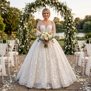 Bride wearing a luxury long sleeve ball gown wedding dress with a transparent illusion neckline and all-over white floral lace appliques at an outdoor garden ceremony.