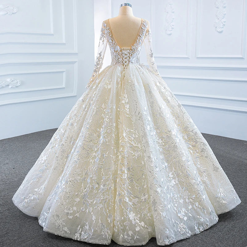 Full back view of a long sleeve bridal gown showcasing a deep V backless design with a ribbon lace-up corset closure and a voluminous tulle skirt.