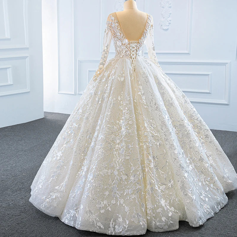 Rear three-quarter profile of a romantic princess wedding dress highlighting the sheer lace sleeves, low-cut corset back, and cascading floral embroidery.