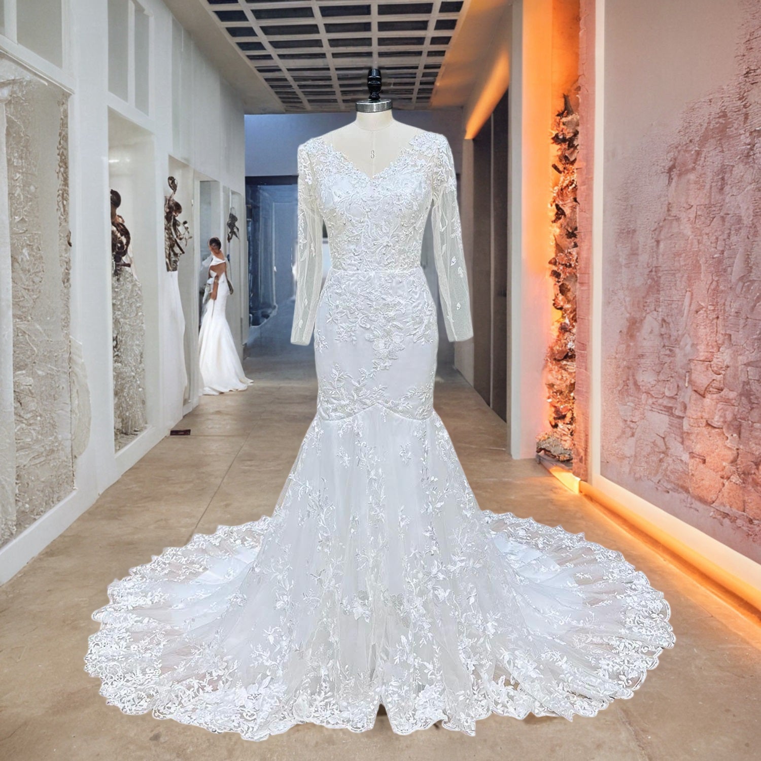 Long sleeve tulle trumpet wedding dress featuring all-over floral lace and sequin beading displayed on a mannequin in a modern boutique hallway.