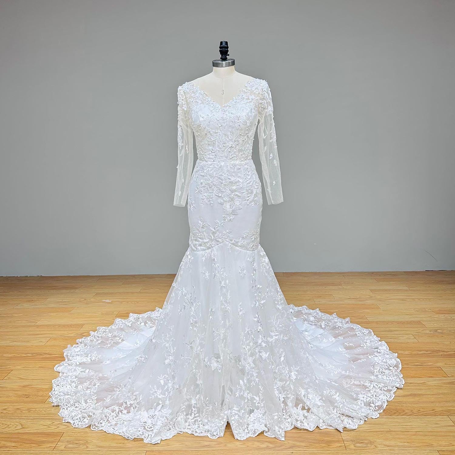 Showing a full front studio view of a white lace and tulle mermaid wedding gown with long sheer sleeves and a V-neckline on a dress form.