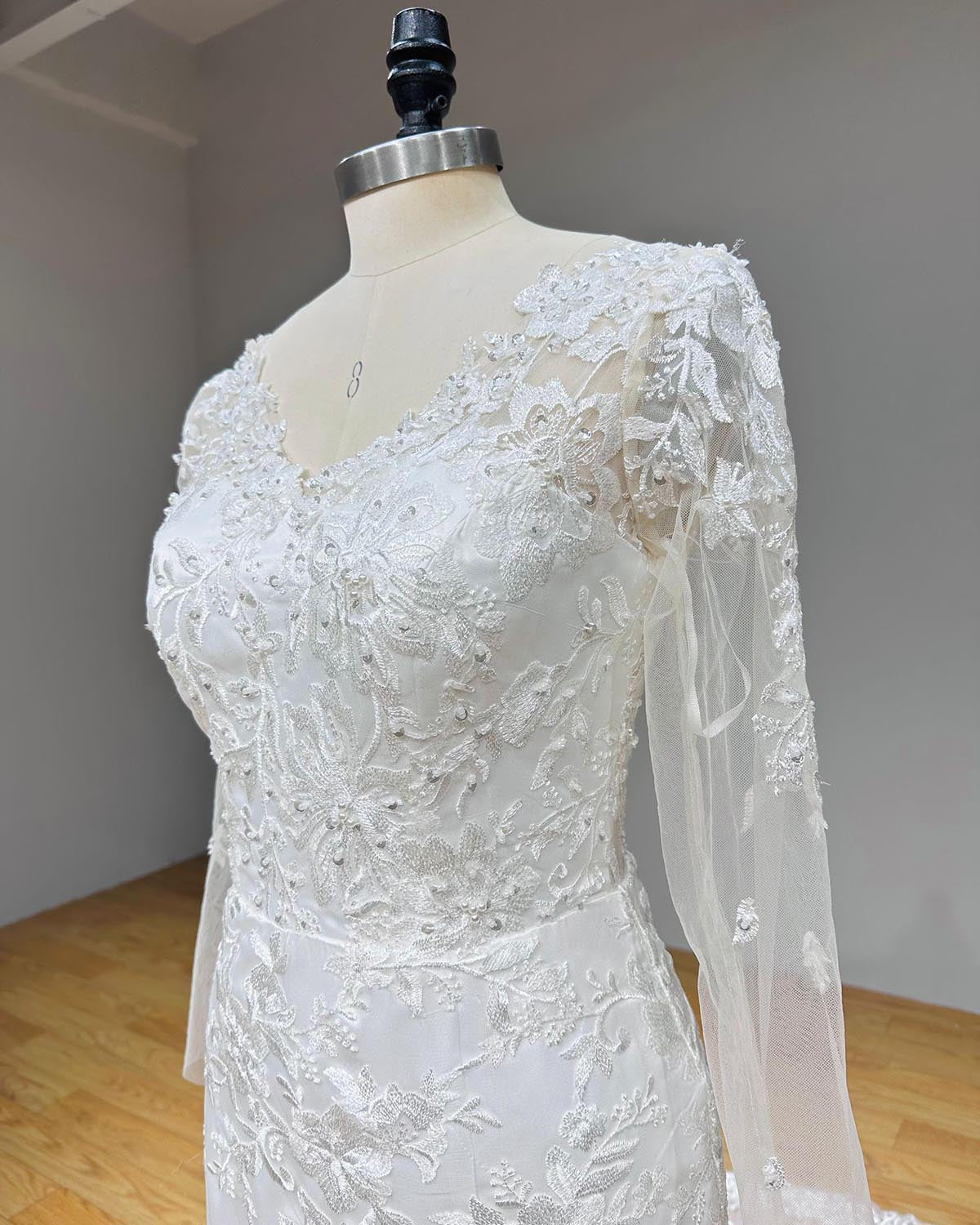 Side profile close-up of a bridal gown bodice showcasing sheer long sleeves with sequined beadwork and romantic floral lace appliqués.