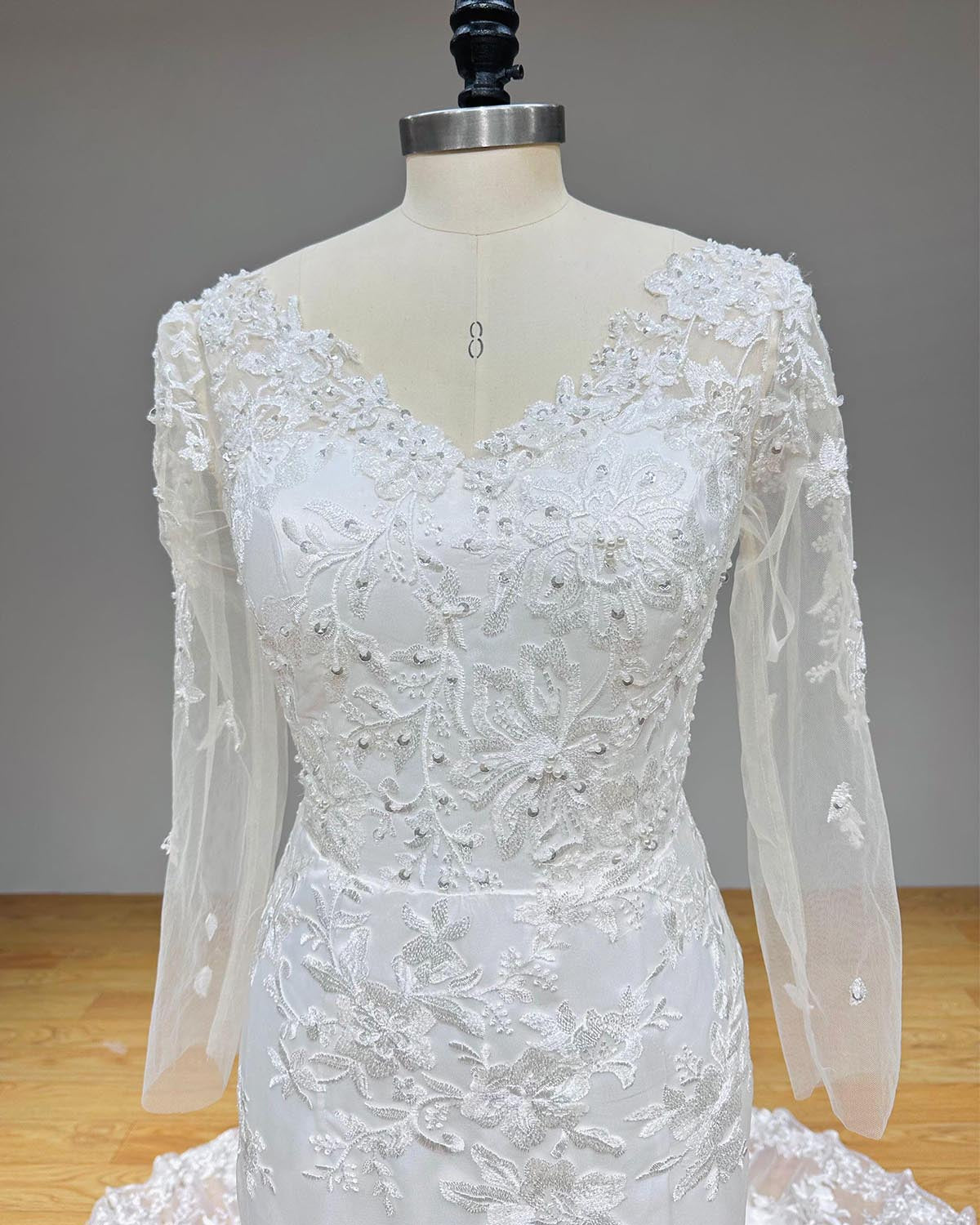 High-resolution front close-up of a V-neckline bridal bodice highlighting intricate white thread embroidery, sequins, and shimmering bead clusters.