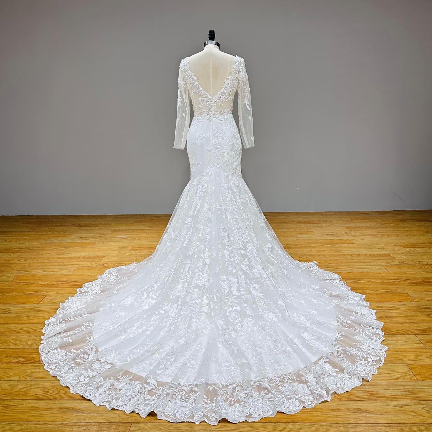 Full-length back studio view of a white tulle mermaid wedding dress on a mannequin, showcasing a sprawling scalloped lace-edge train.