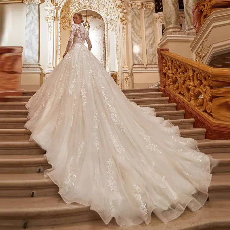 A bride posing on a grand staircase in a luxurious long-sleeve A-line wedding gown with an extensive lace-detailed train.