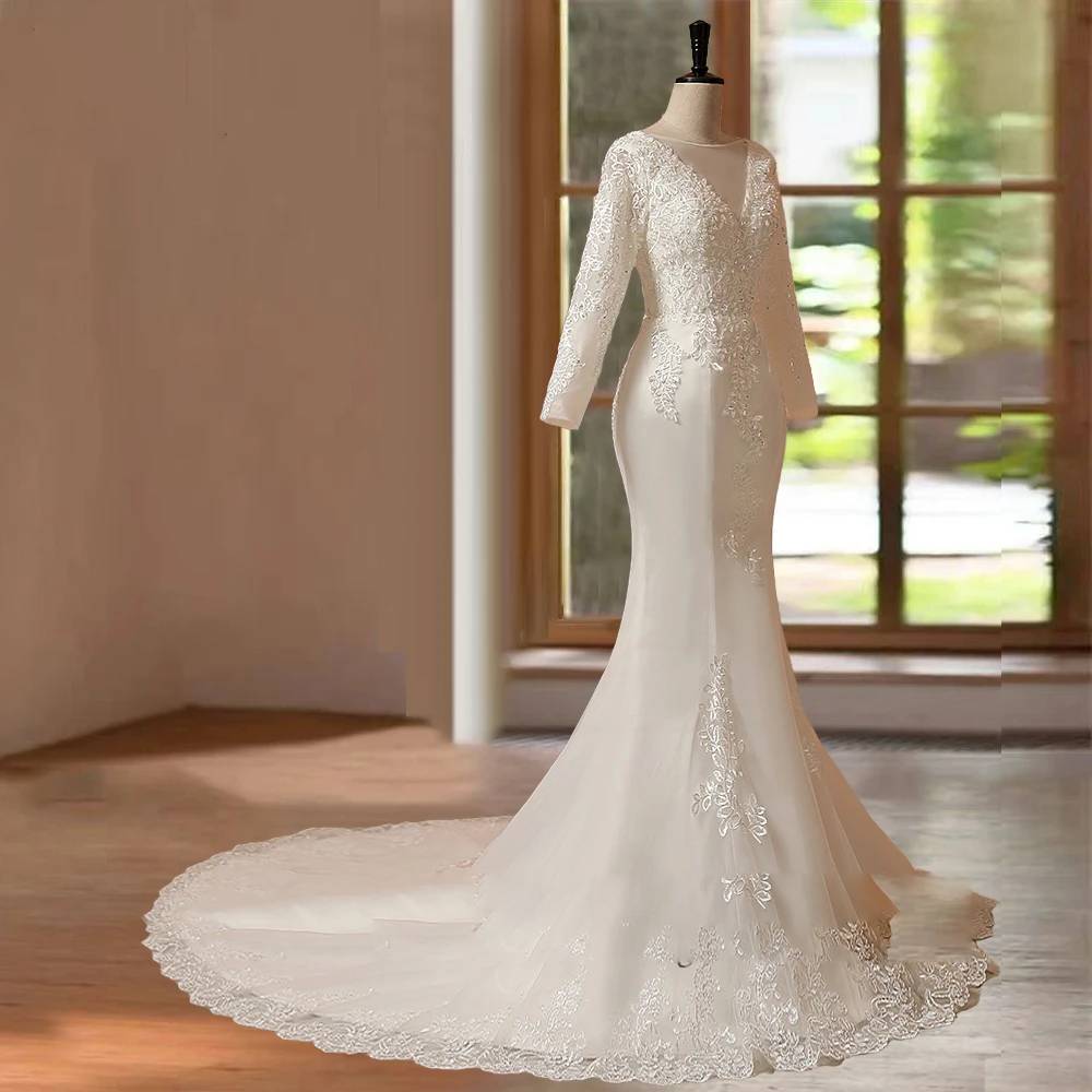 Side profile view of a long sleeve mermaid bridal gown displayed on a studio mannequin, capturing the form-fitting lace bodice and the graceful flow of the extended tulle train.