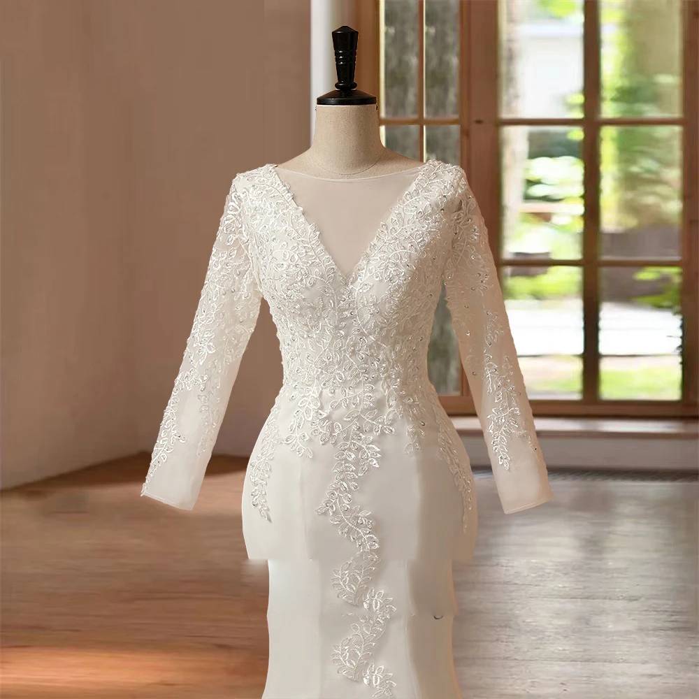 Close-up bodice detail of a long sleeve O-neck mermaid wedding dress on a mannequin, focusing on the sheer illusion neckline, dense floral lace embroidery, and delicate long sleeves.