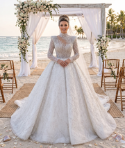 Full-length front view of a model wearing a luxurious high neck sequined wedding dress featuring sheer illusion long sleeves, intricate floral lace appliques, and a shimmering royal ball gown skirt.