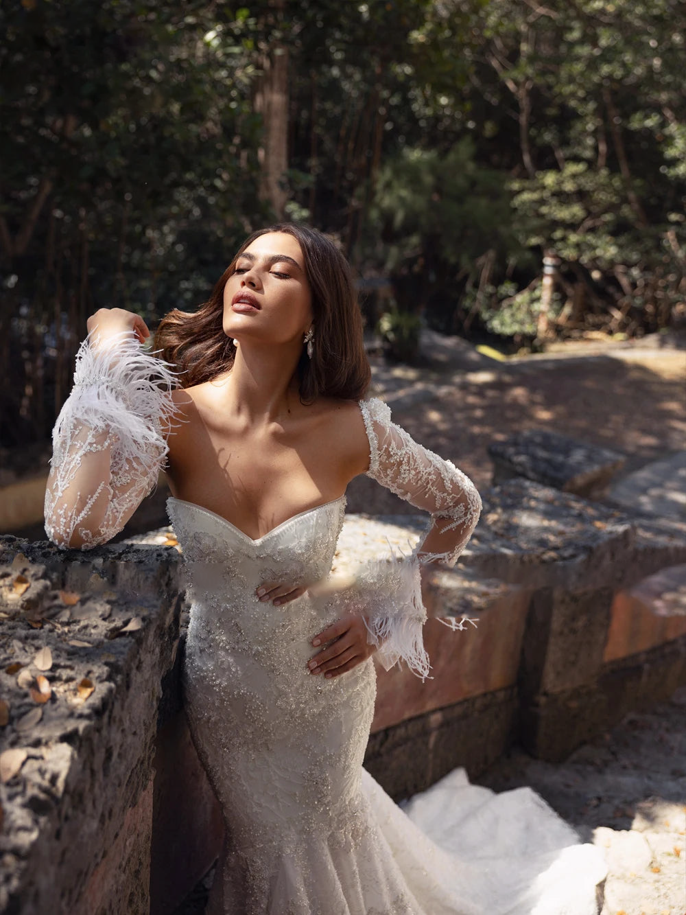 Back view of a luxurious mermaid bridal dress highlighting a low-cut back design, contoured hips, and a sweeping lace court train trailing down stone steps.