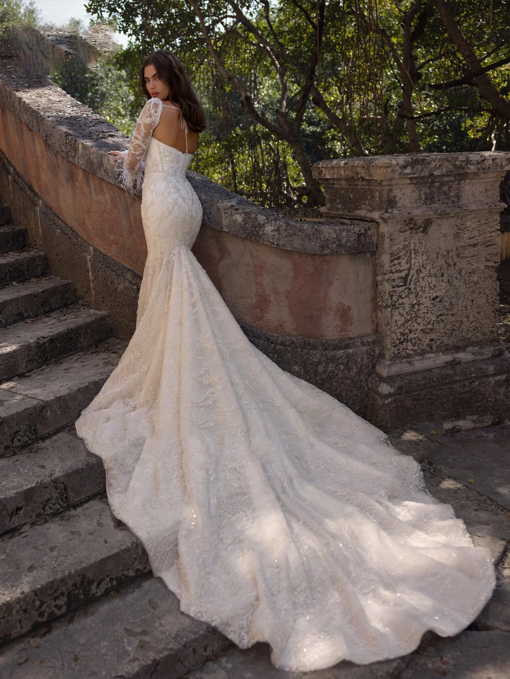 Alternative side view of a sparkling lace bridal gown fanned out near an estate walkway, emphasizing the elegant flow of the floor-length court train overlay.