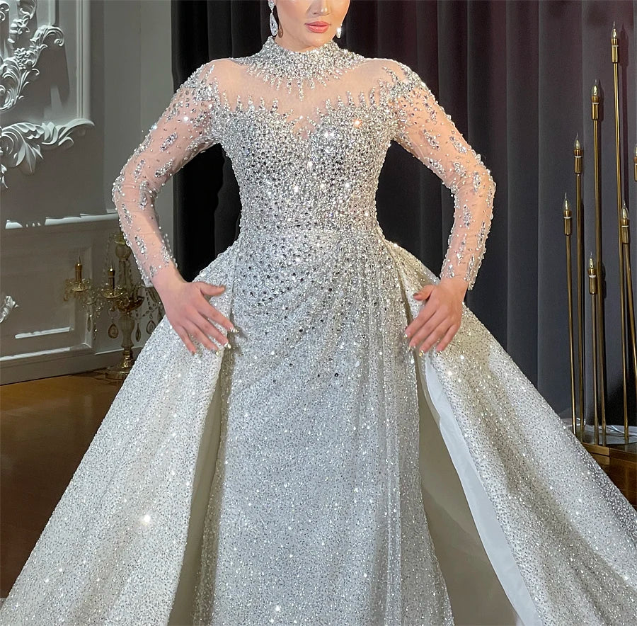 Close-up detail of a heavily beaded bridal gown bodice, showcasing the intricate hand-stitched crystal patterns and the seamless attachment of the voluminous detachable train.