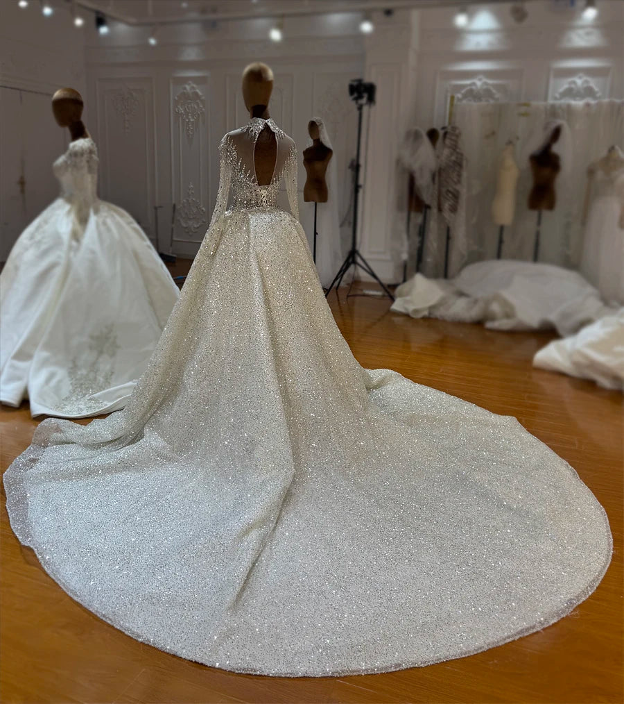 A grand back perspective of the luxury 2-in-1 bridal gown with the overskirt attached, displaying an expansive cathedral-length train covered in reflective sequins and beads.