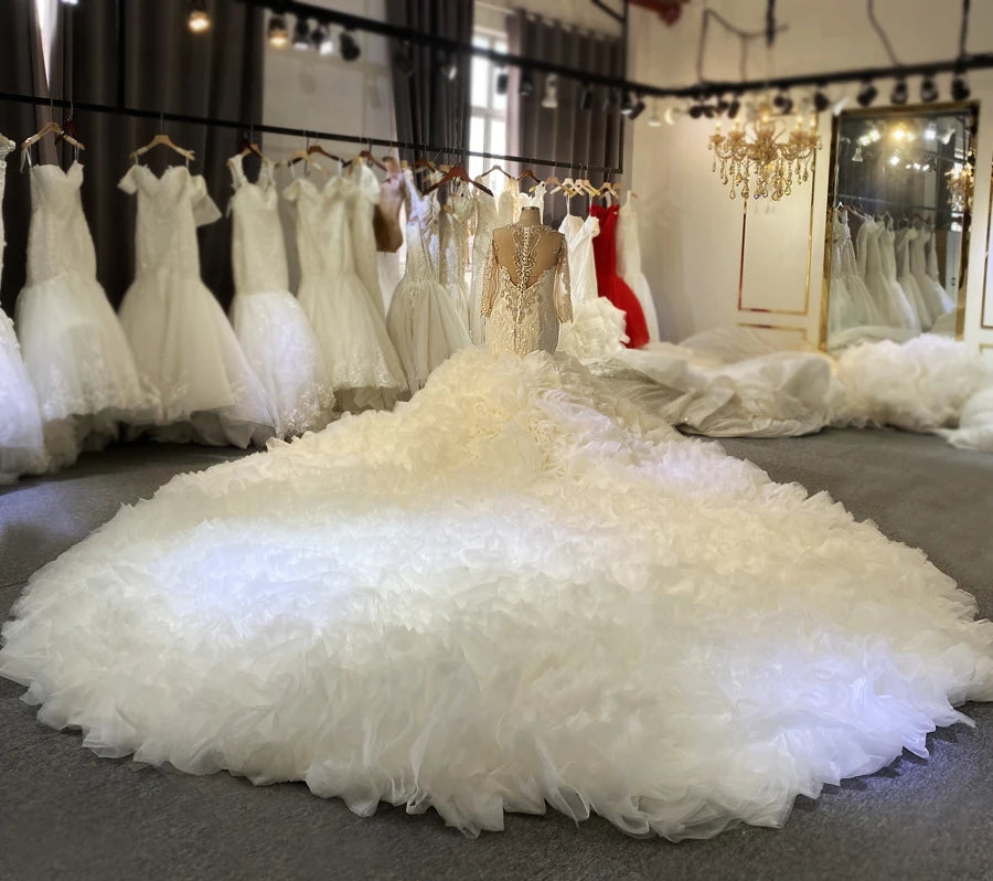 Real work photo of an African bride wearing a luxury 2-in-1 mermaid wedding dress with long sleeves and a grand shimmering ruffled overskirt.