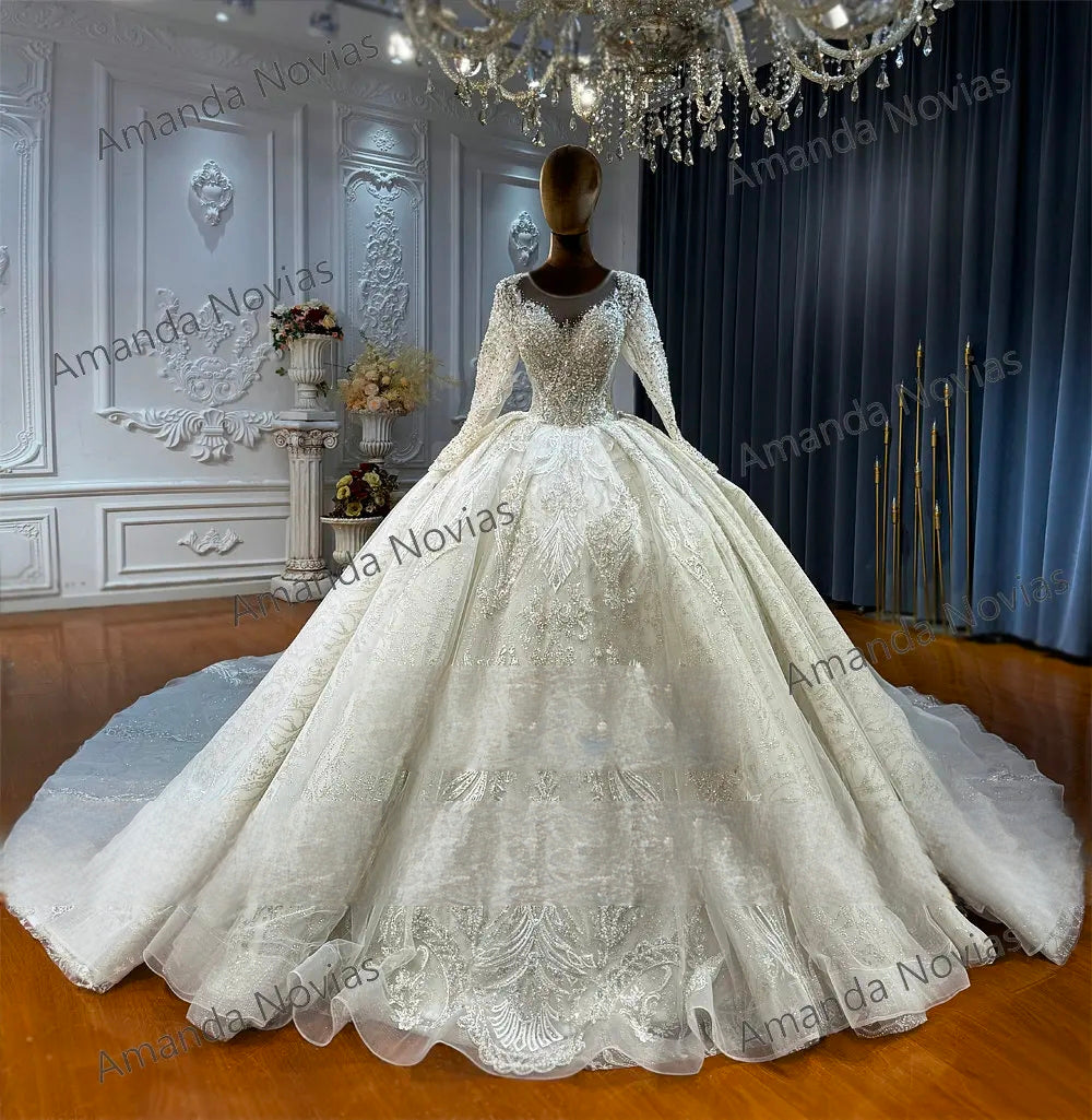 Majestic front perspective of a sparkling long-sleeve wedding gown with a full ballroom silhouette, illustrating the grand scale of the train and the sophisticated texture of the beaded lace fabric.