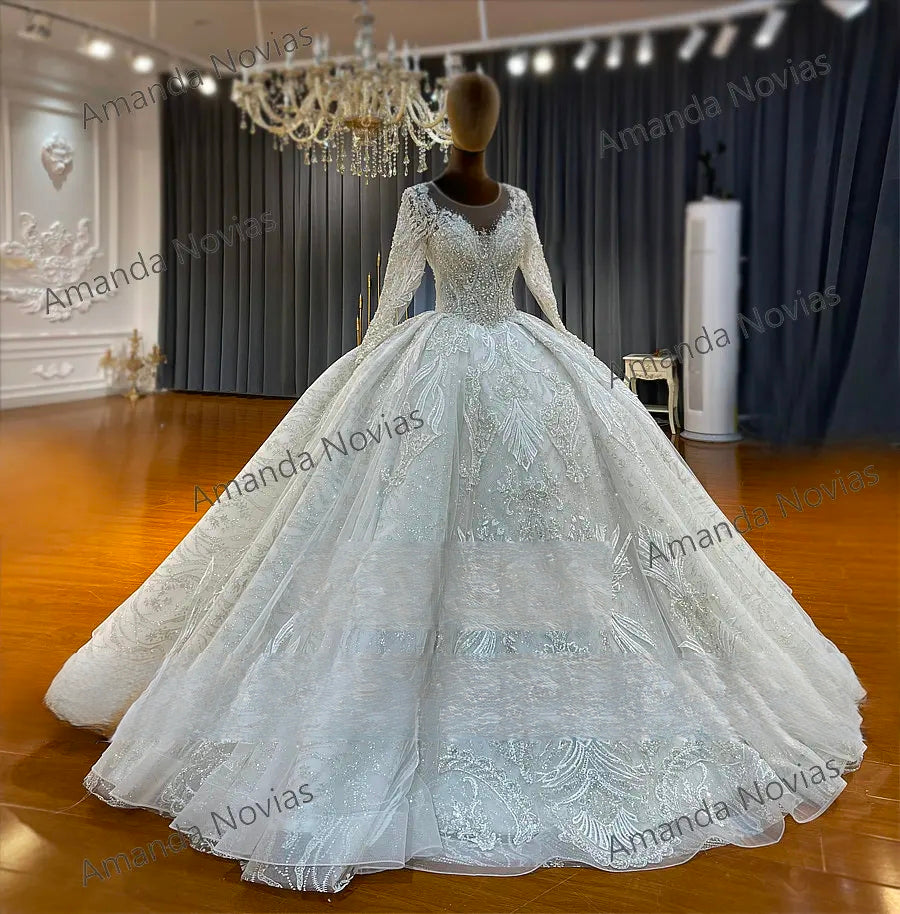 Wide-angle showroom view of an off-white bridal ball gown, emphasizing the massive, shimmering cathedral-length skirt and the regal long-sleeved silhouette.