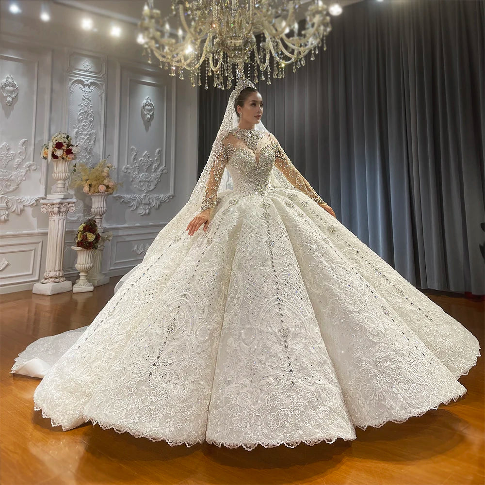 Full front view of a luxury ball gown wedding dress with a square neckline and long sleeves, featuring heavy rhinestone embellishments and a voluminous shimmering skirt on a mannequin.