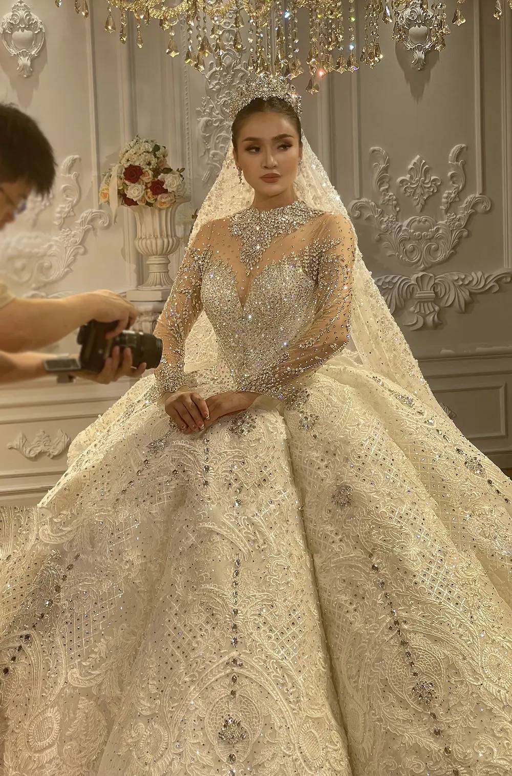Rear view of a shimmering bridal ball gown showcasing an elegant lace-up back and an expansive, sparkling cathedral-length train in a luxury bridal studio.