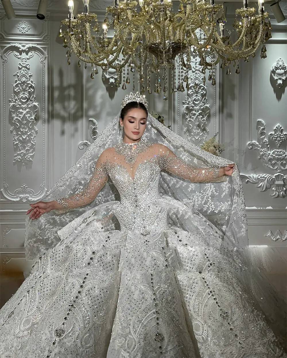 Close-up detail of a bridal gown bodice highlighting the dense hand-beaded rhinestones, silver crystal patterns, and delicate sheer long sleeves.