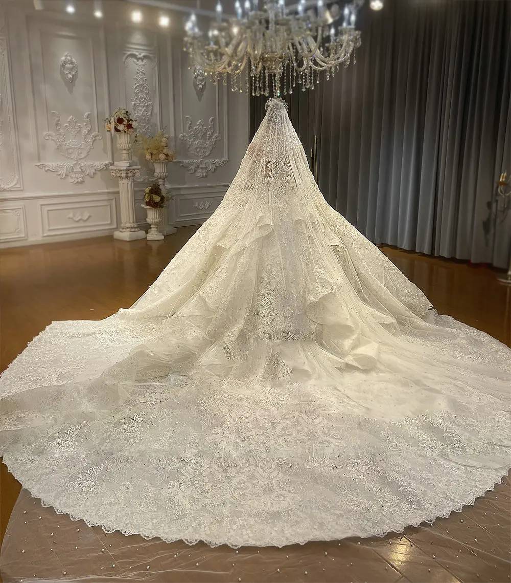 Side-angle view of a grand royal wedding dress on a mannequin, emphasizing the wide-sweep shimmering skirt and the majestic silhouette of the rhinestone-embellished ball gown.