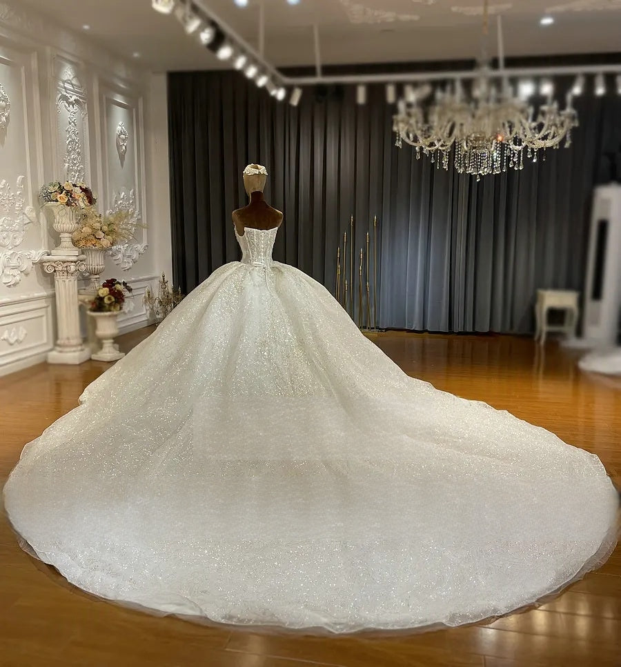 Breathtaking rear view of a luxury beaded mermaid wedding gown on a mannequin, showcasing the immense, shimmering cathedral-length train spread across a showroom floor.