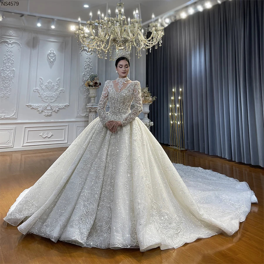 Full front view of a model wearing a luxury beaded ball gown wedding dress with long sleeves and an elegant removable high-neck illusion collar featuring a massive cathedral train.