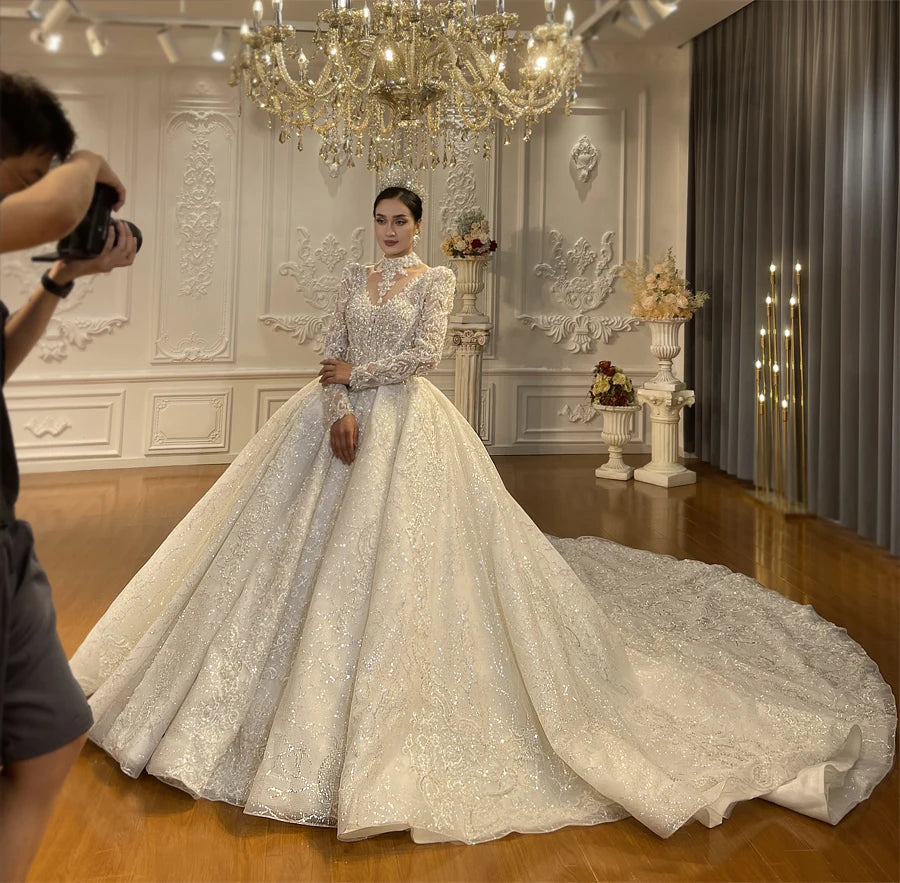 Side-profile view of a sparkling long-sleeved bridal gown with heavy crystal beading and a voluminous flared skirt in a luxury bridal showroom.