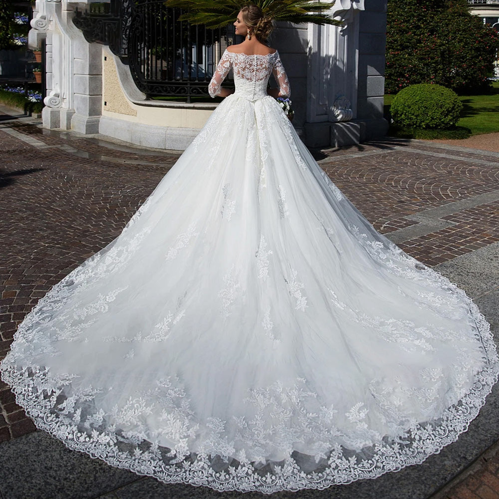 Back view of a vintage-style A-line bridal gown, showcasing a detailed lace boat neck, long sweeping train, and intricate button-down back.