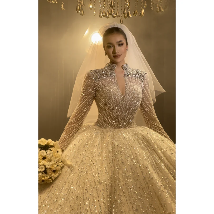 Close-up front view of a luxury bridal ball gown with a square neckline and long sleeves, featuring dense silver crystal beading and a royal bridal tiara.